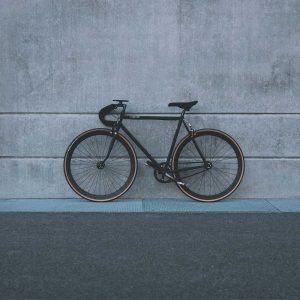 Black single-speed bike with drop handlebars and tan-wall tyres against a concrete wall