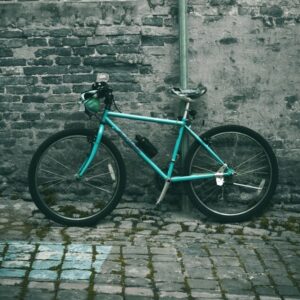 Teal mountain bike with knobby tyres leaning against a brick wall